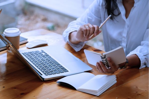 Persona adulta combinando estudio y trabajo frente a un ordenador con apuntes de oposición TIC.
