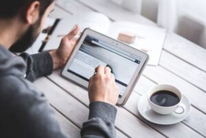 Persona consultando en una tablet los distintos tipos de boletines oficiales con una taza de café al lado
