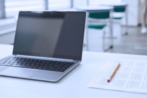 Portátil y hoja de examen tipo test en aula vacía, símbolo de preparación para oposiciones TIC del Estado