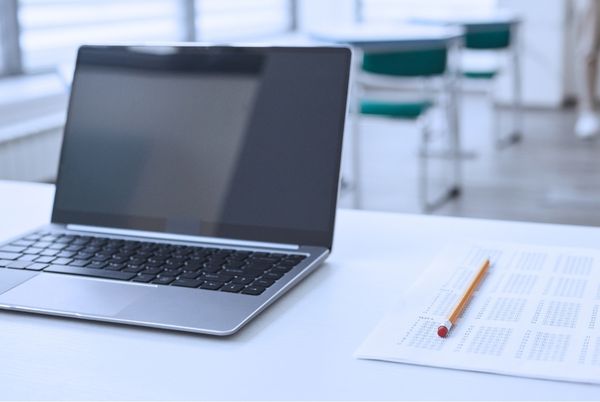 Portátil y hoja de examen tipo test en aula vacía, símbolo de preparación para oposiciones TIC del Estado