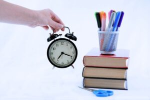 Reloj despertador junto a libros y material de estudio, simbolizando el tiempo para preparar una oposición TIC