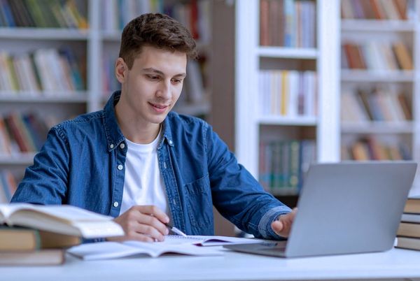 Persona estudiando con ordenador y libros en una biblioteca, ejemplo de motivación para estudiar.