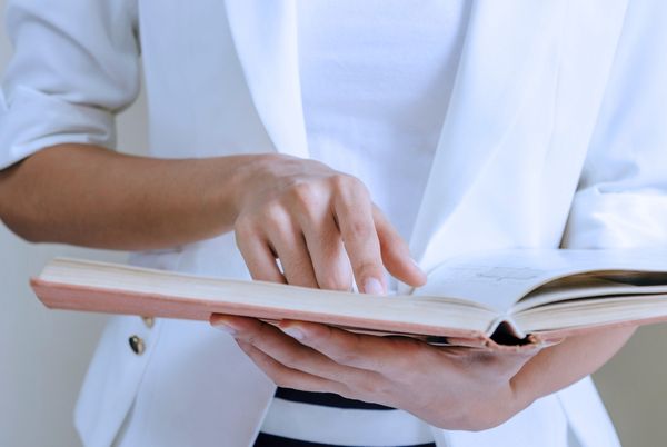 Persona consultando un libro abierto como material de apoyo para el estudio de administración electrónica.