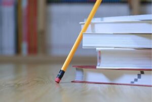 Lápiz apoyado junto a una pila de libros usados para estudiar resúmenes de forma efectiva.