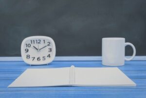 Reloj, cuaderno abierto y taza sobre una mesa, imagen para qué priorizar cuando no puedes estudiar todo en oposición TIC