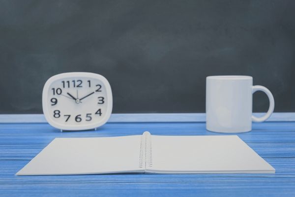 Reloj, cuaderno abierto y taza sobre una mesa, imagen para qué priorizar cuando no puedes estudiar todo en oposición TIC