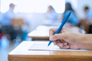 Aspirante realizando un examen de oposición TIC en aula bajo evaluación del tribunal calificador